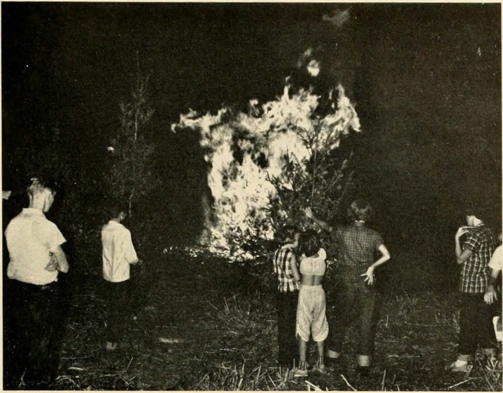 Black and white photograph from a monthly magazine the Panama Canal Review that shows the backs of seven children as the look at a Christmas tree bonfire in the Panama Canal Zone in 1955.