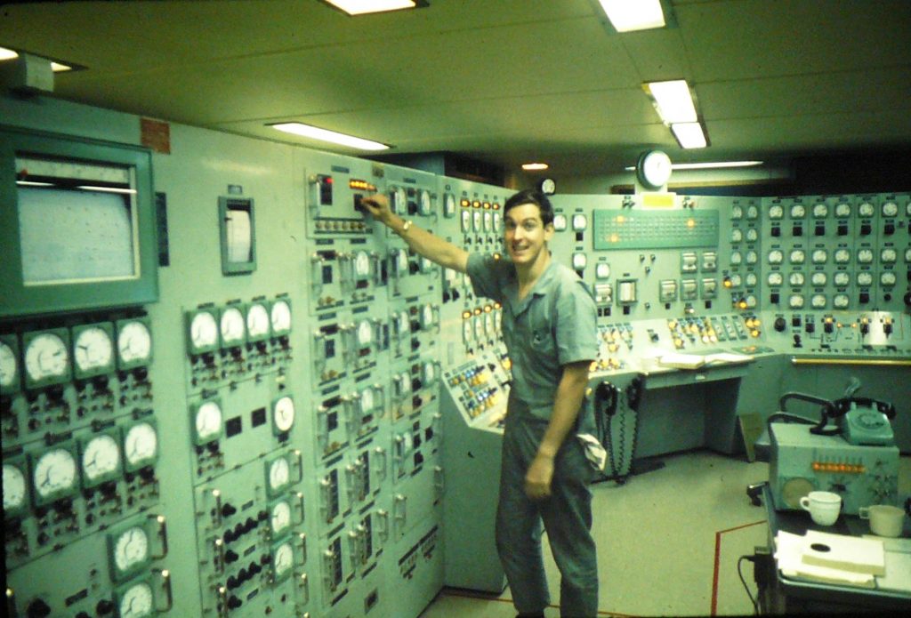 Man smiling at the camera, standing in the MH-1A nuclear reactor control room.