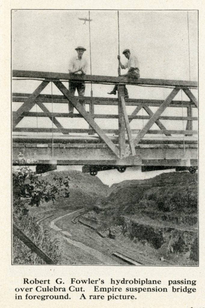 Two men stand on the suspension bridge over the Culebra Cut portion of the Panama Canal construction. Robert Fowler's airplane is behind them in the sky.