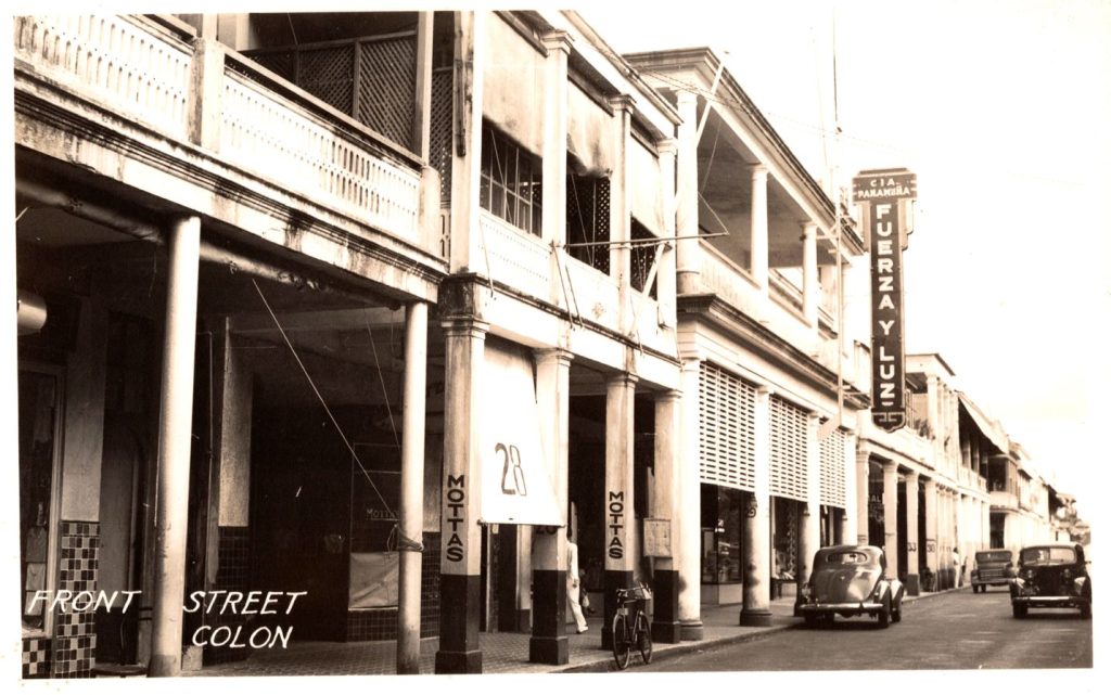 Black and white photo of cars on Front Street in Colon, Republic of Panama. The image shows left-hand driving.